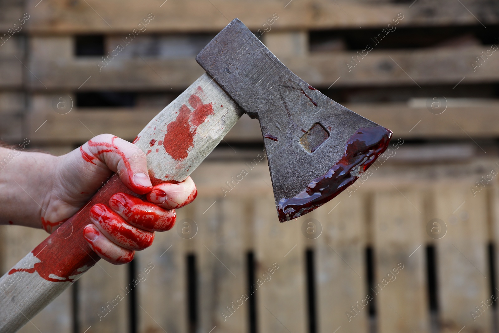 Photo of Man holding bloody axe outdoors, closeup view