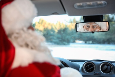 Authentic Santa Claus looking into rear view mirror inside of car