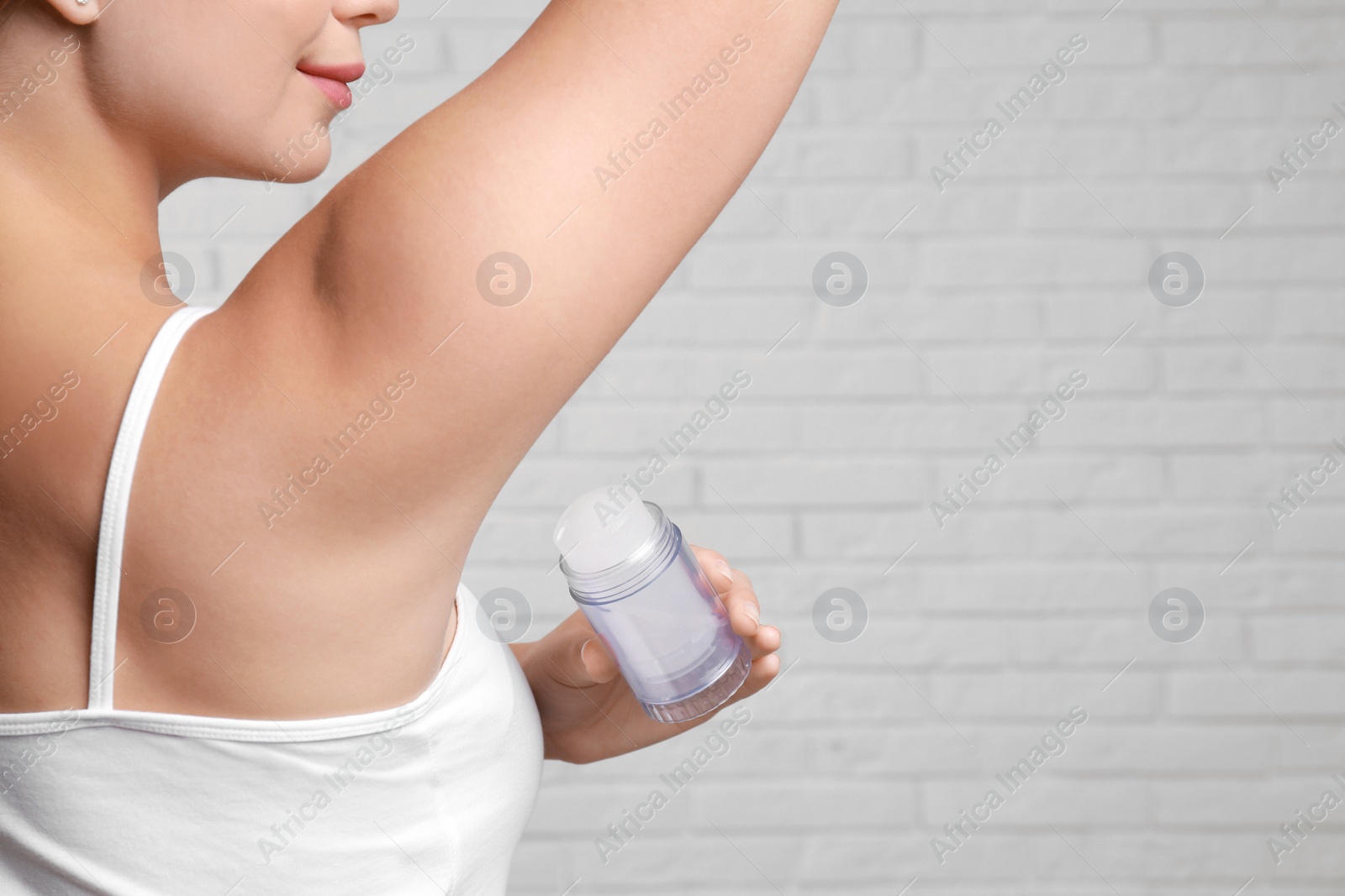 Photo of Young woman applying crystal alum deodorant to armpit against brick wall, closeup. Space for text