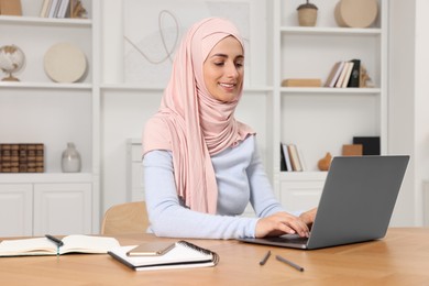 Photo of Muslim woman using laptop at wooden table in room