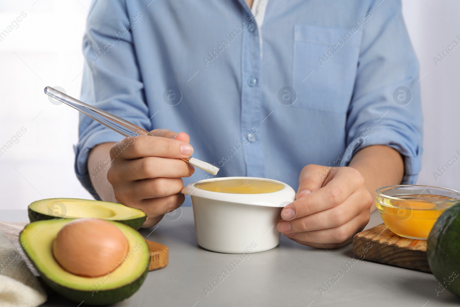 Photo of Woman with handmade face mask, brush and ingredients at grey table, closeup