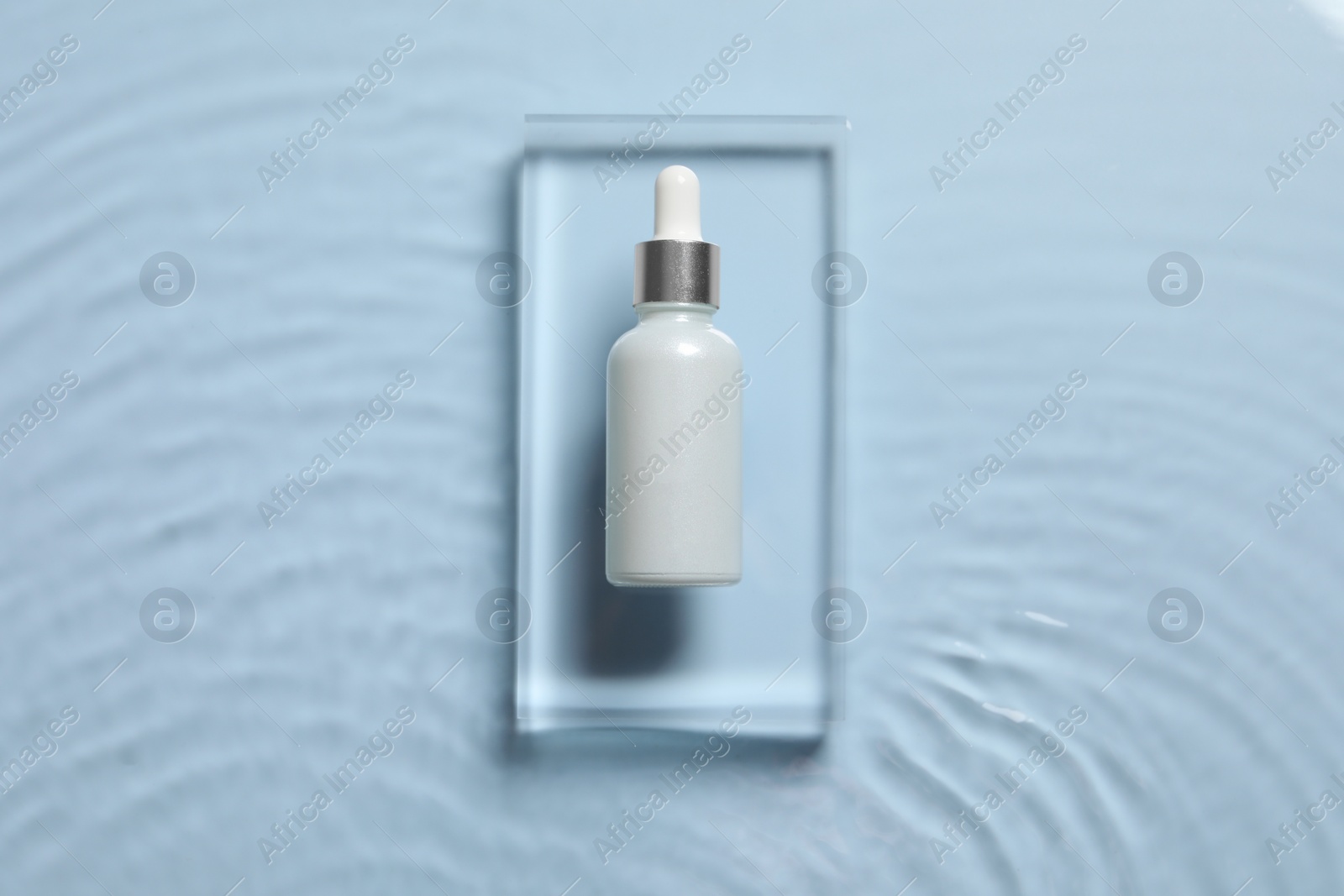 Photo of Bottle of cosmetic serum and water on light blue background, top view