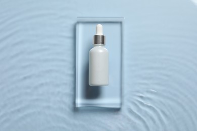 Photo of Bottle of cosmetic serum and water on light blue background, top view