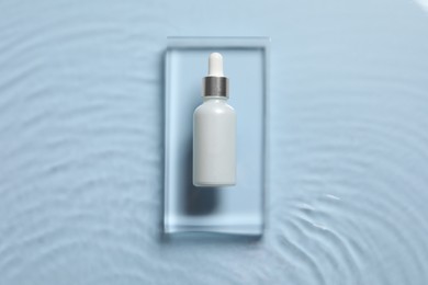 Bottle of cosmetic serum and water on light blue background, top view