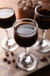 Photo of Shot glasses with coffee liqueur and beans on wooden table, closeup