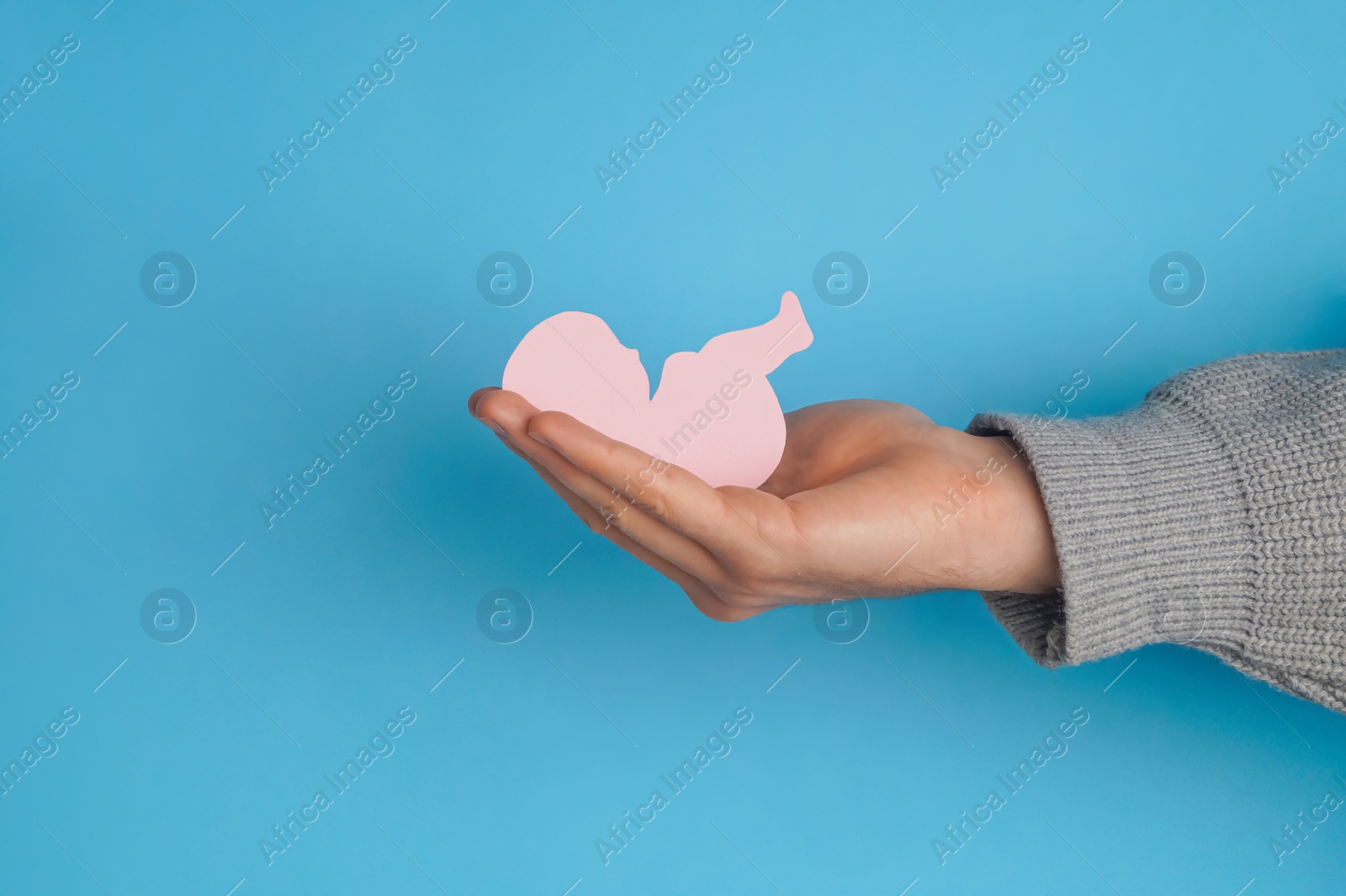 Photo of Female health. Man holding newborn paper figure on light blue background, closeup of hand