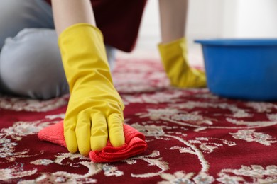 Photo of Woman in rubber gloves cleaning carpet with rag indoors, closeup. Space for text