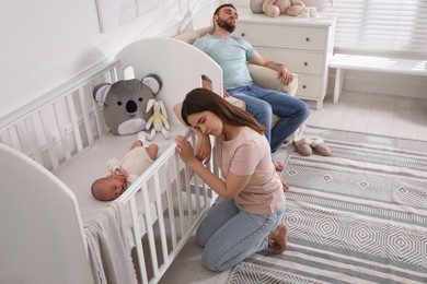 Tired young parents and their baby sleeping in children's room