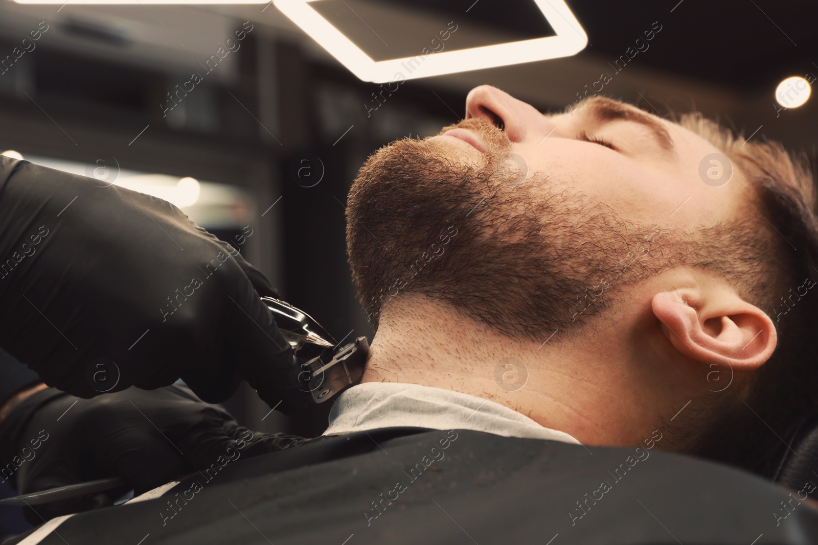 Photo of Professional hairdresser working with client in barbershop, closeup 