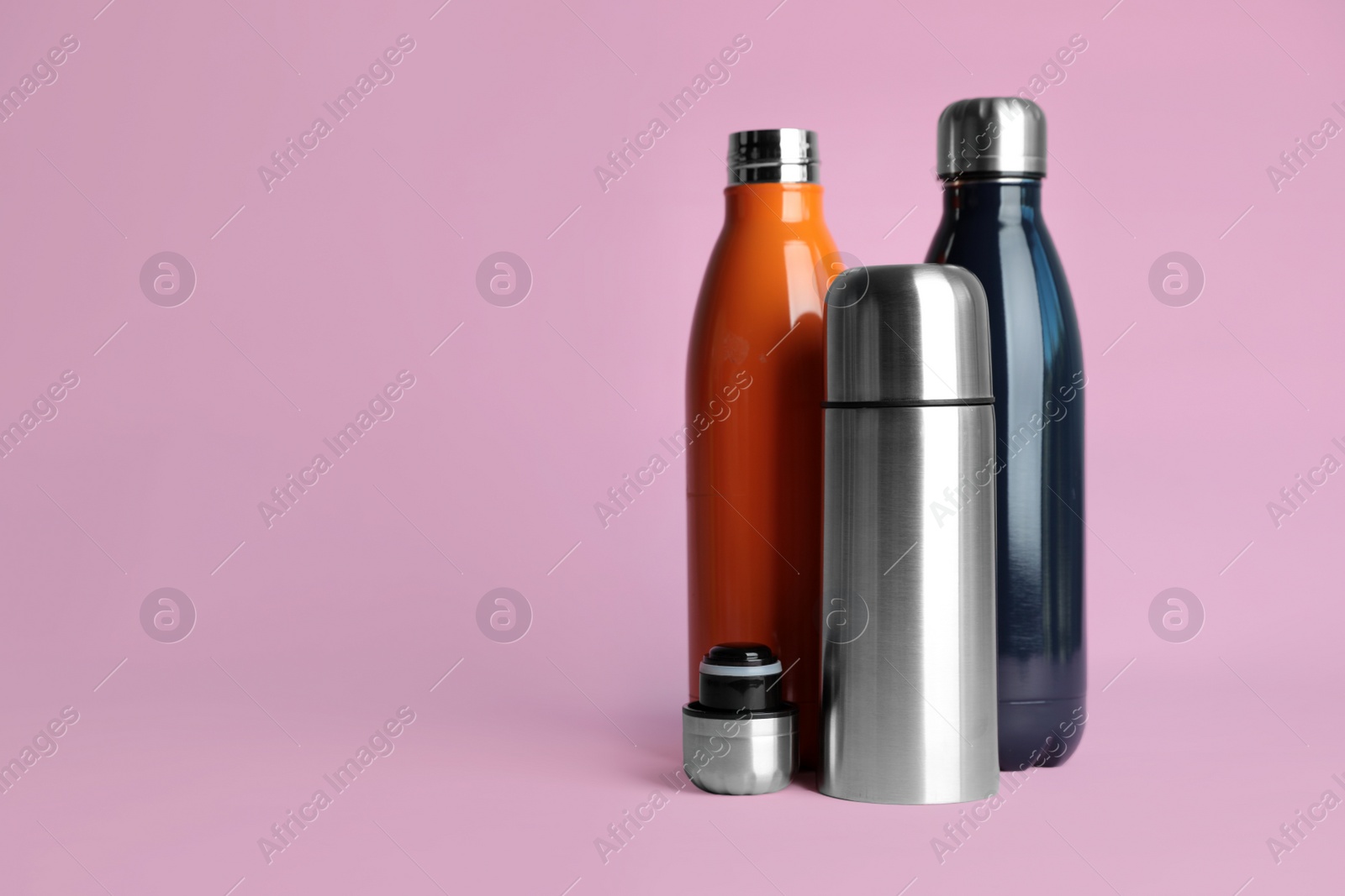 Photo of Stylish thermo bottles on pink background, space for text