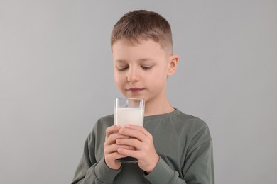 Cute boy with glass of fresh milk on light grey background