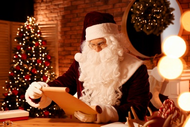 Photo of Santa Claus reading wish list at table indoors