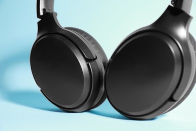 Photo of Modern wireless headphones on light blue background, closeup