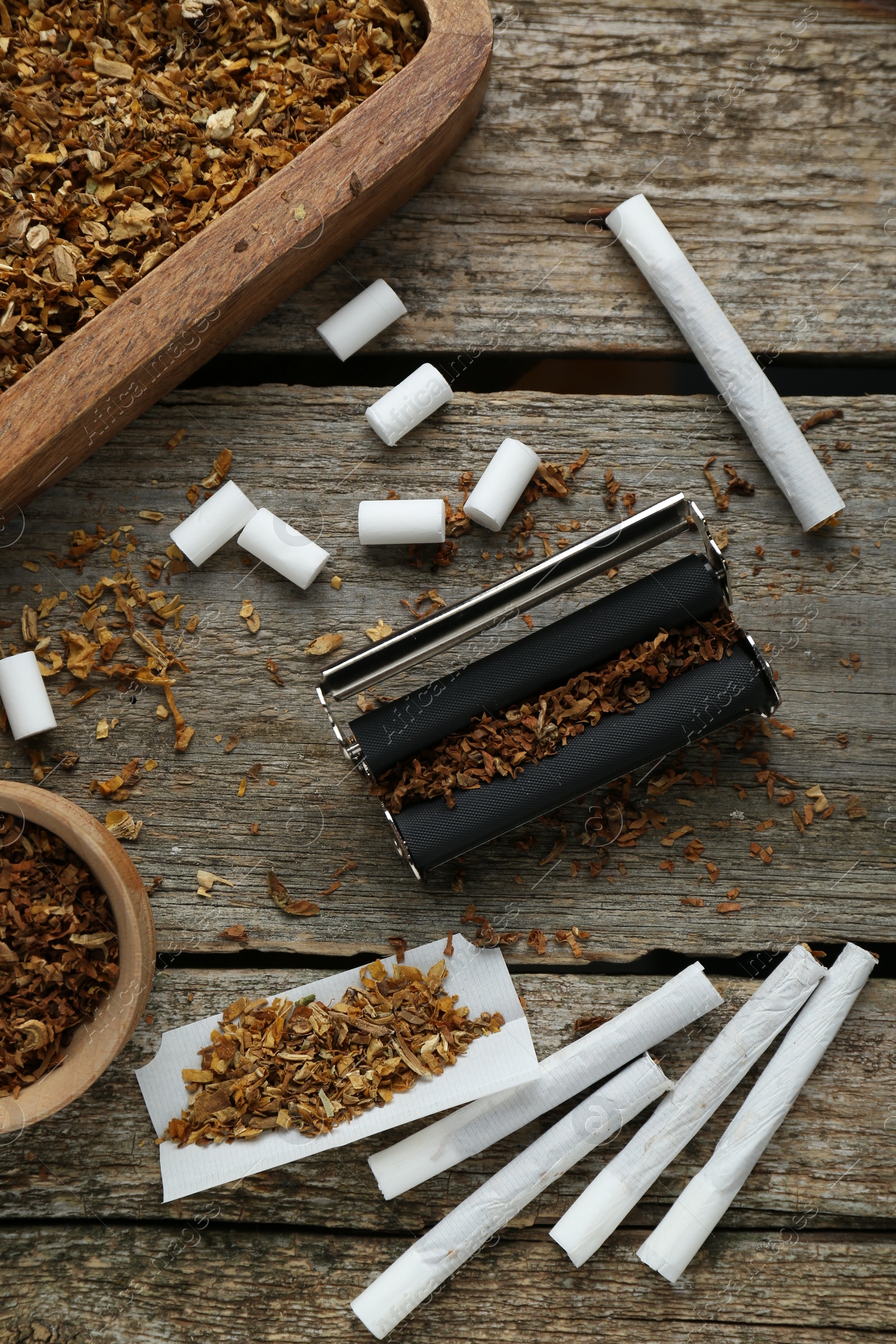 Photo of Flat lay composition with roller and tobacco on old wooden table. Making hand rolled cigarettes