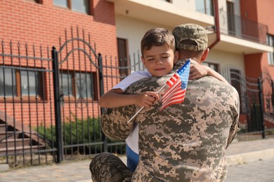 Soldier and his little son with flag of USA hugging outdoors