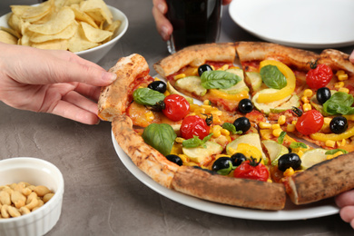 Photo of Women taking slices of delicious vegetable pizza at grey table, closeup