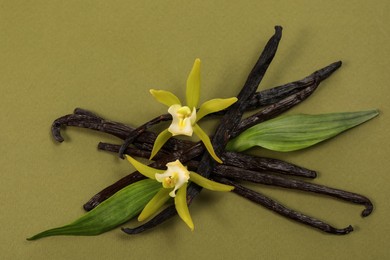 Photo of Vanilla pods, beautiful flowers and green leaves on olive color background, top view