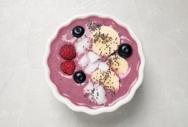 Delicious acai smoothie with fruits and coconut chips in dessert bowl on grey table, top view