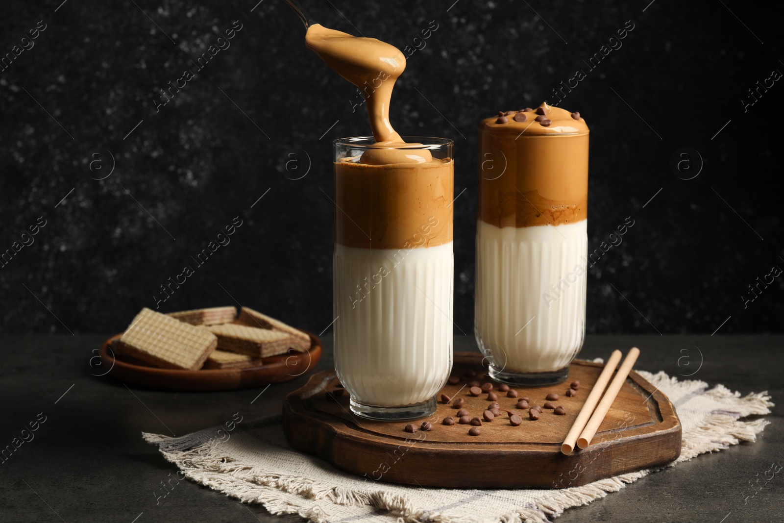 Photo of Pouring cream for dalgona coffee into glass on dark table