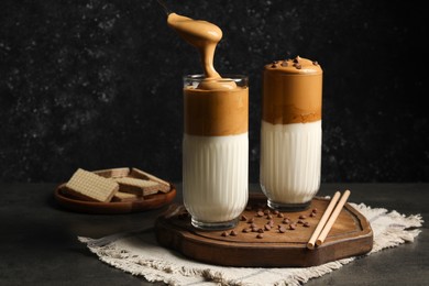 Photo of Pouring cream for dalgona coffee into glass on dark table