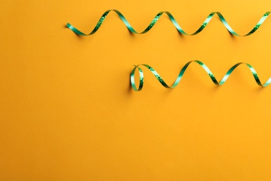 Photo of Shiny green serpentine streamers on orange background, flat lay. Space for text