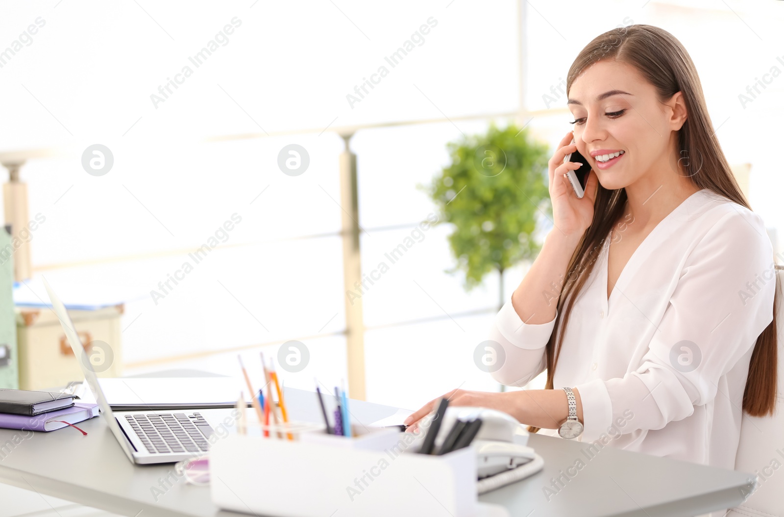 Photo of Young woman talking on phone at workplace