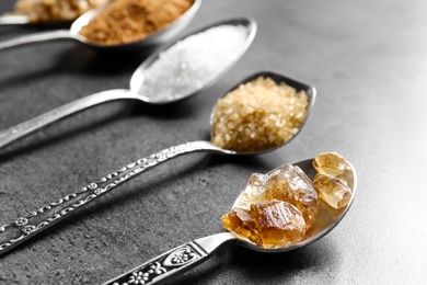 Spoons with various kinds of sugar on grey background