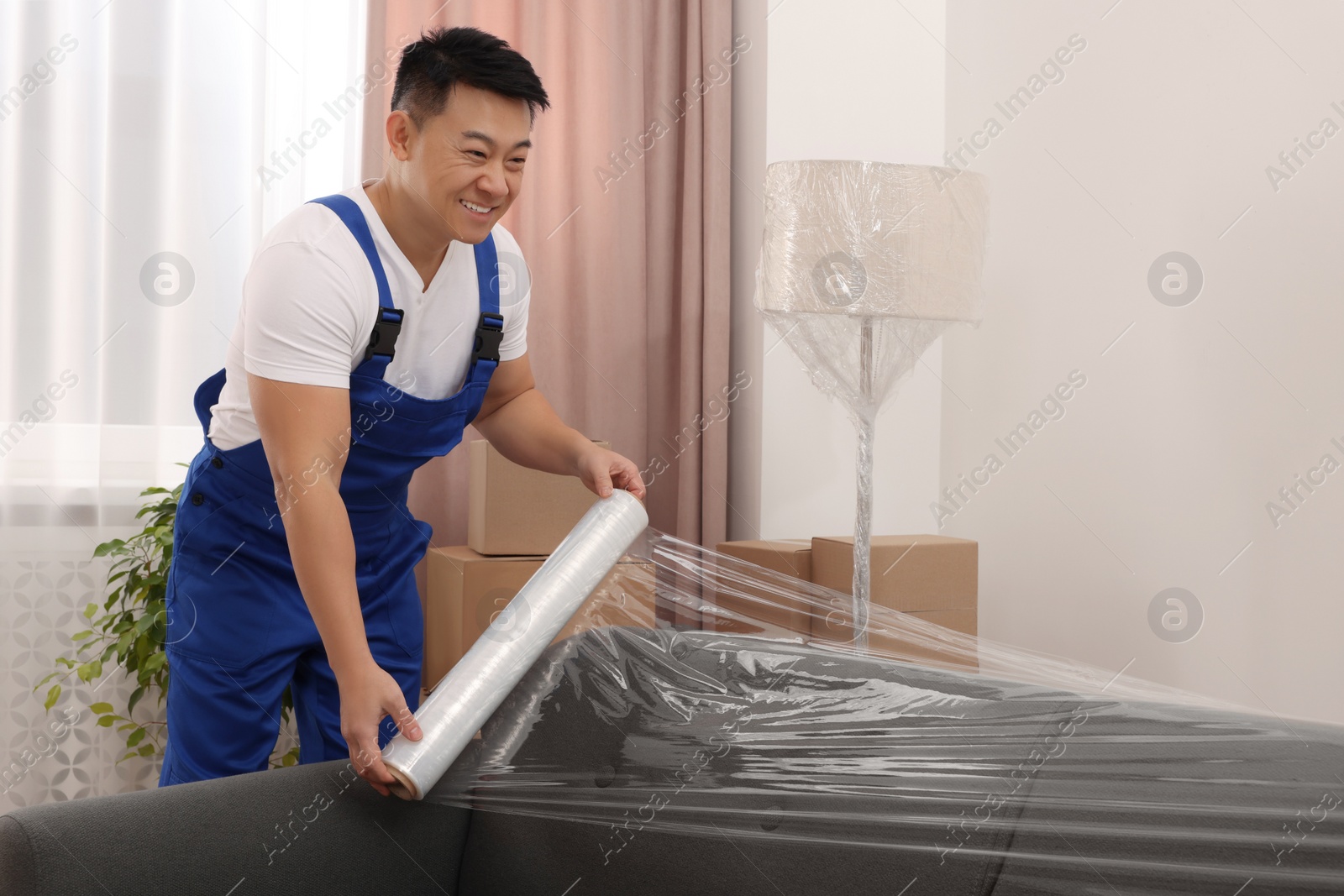 Photo of Worker wrapping sofa in stretch film indoors