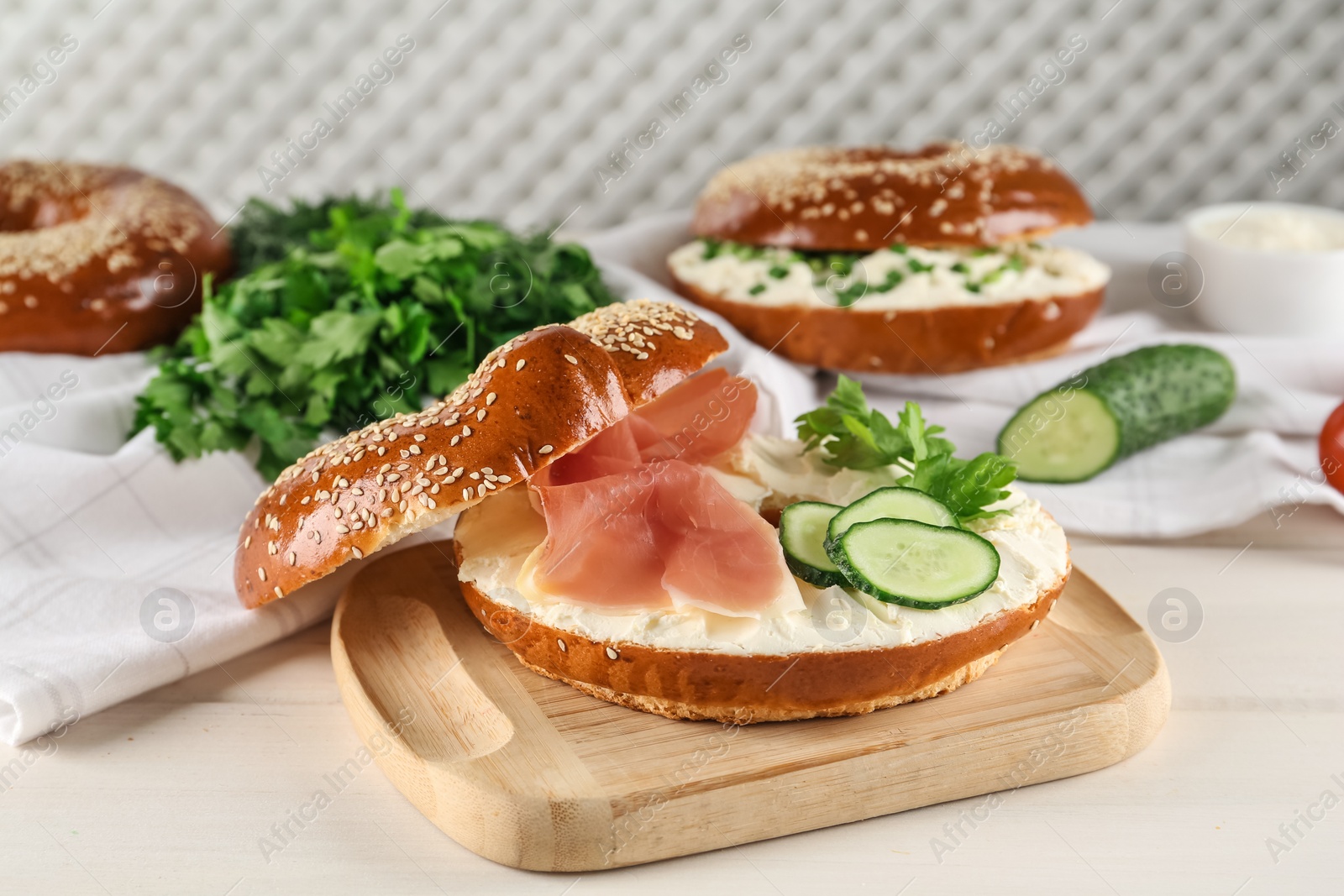 Photo of Delicious bagel with cream cheese, jamon, cucumber and parsley on white wooden table