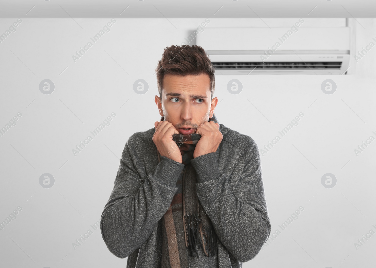 Image of Man suffering from cold in room with air conditioner on white wall