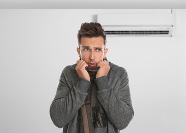 Man suffering from cold in room with air conditioner on white wall