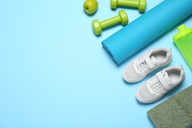 Photo of Exercise mat, dumbbells, apple, towel, shaker and shoes on light blue background, flat lay. Space for text
