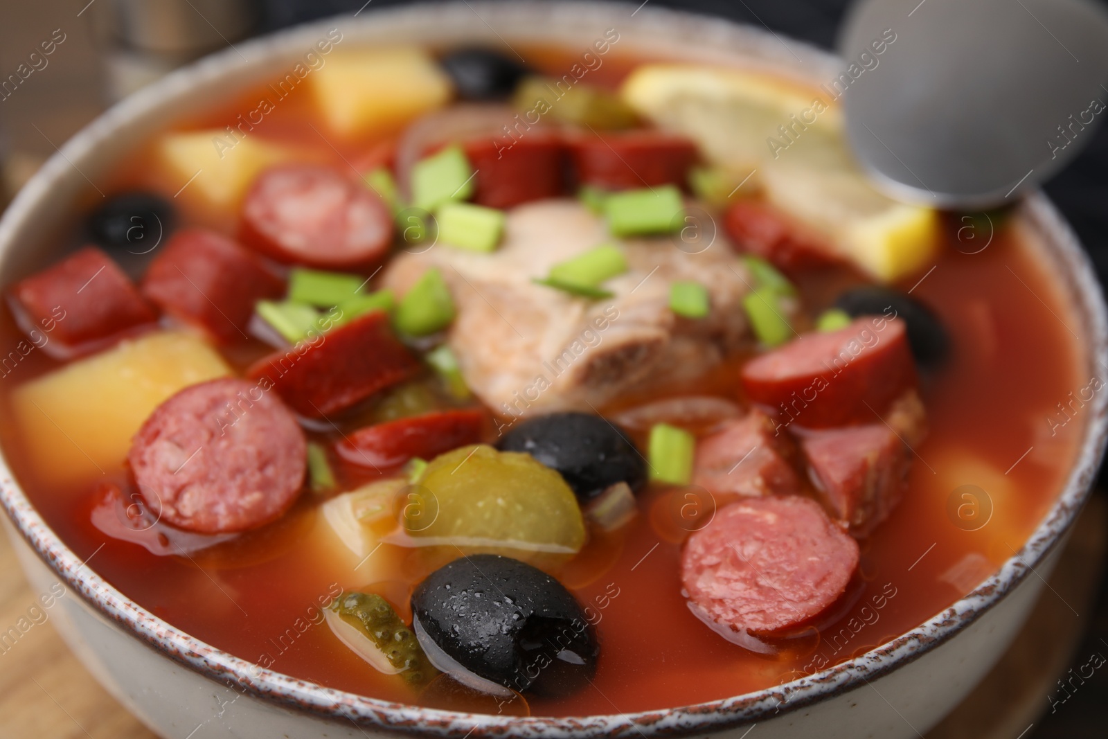 Photo of Meat solyanka soup with thin dry smoked sausages in bowl, closeup