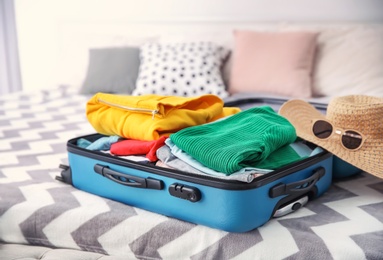 Open suitcase with different personal stuff on bed