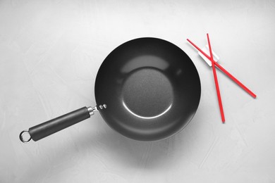 Photo of Empty iron wok and chopsticks on grey table, flat lay