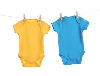 Photo of Colorful baby onesies hanging on clothes line against white background. Laundry day