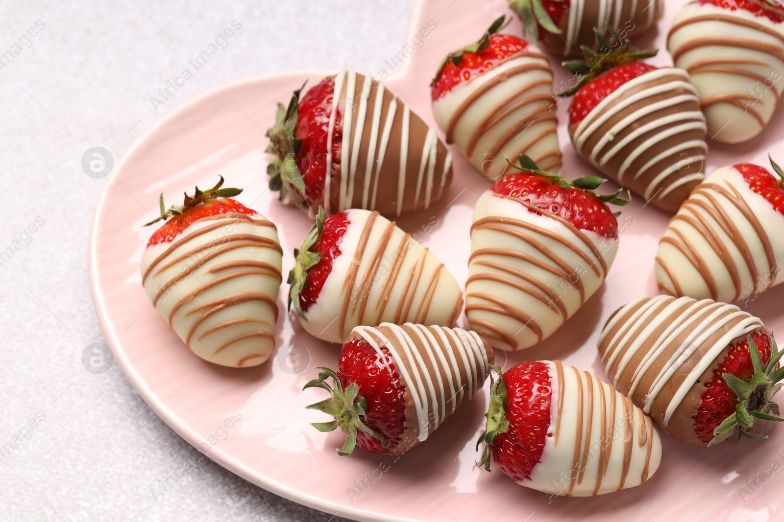 Photo of Heart shaped plate with delicious chocolate covered strawberries on light table, closeup