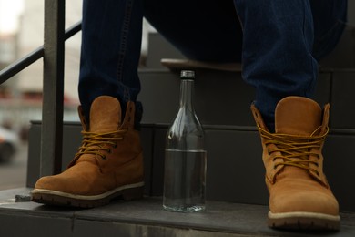 Photo of Addicted man with alcoholic drink on stairs outdoors, closeup