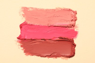 Photo of Smears of beautiful lipsticks on beige background, top view