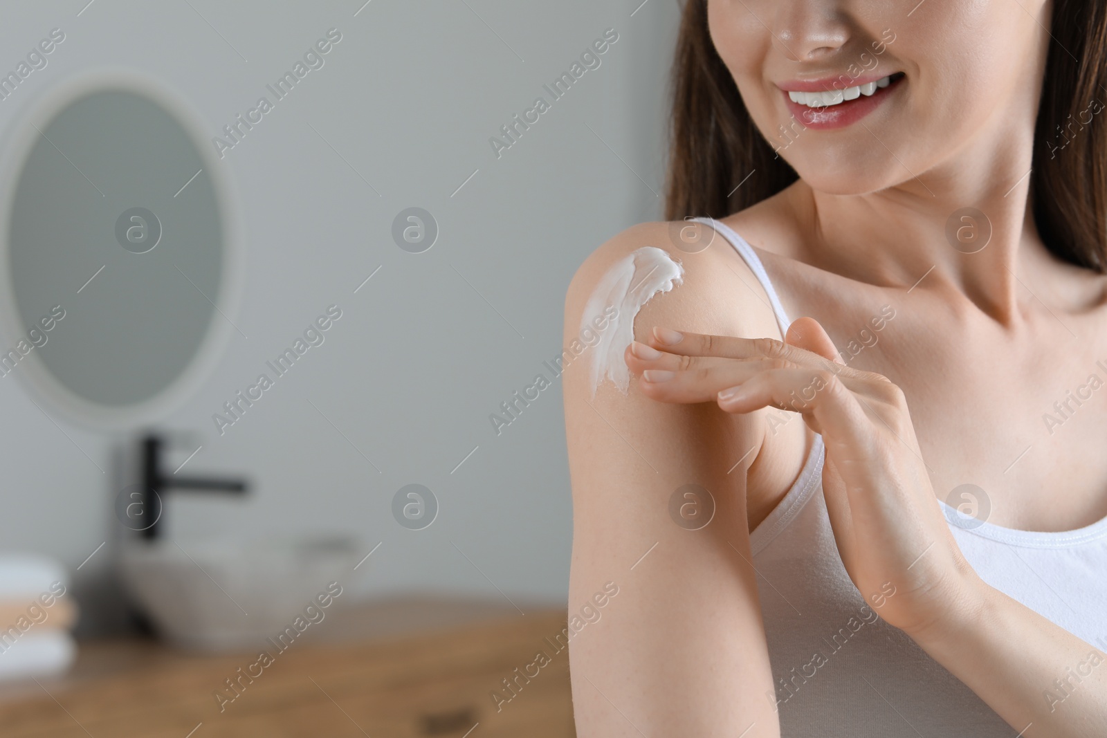 Photo of Woman applying body cream onto shoulder in bathroom, closeup. Space for text