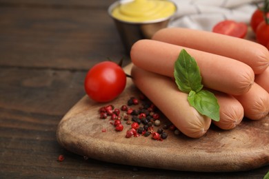 Photo of Delicious boiled sausages, tomato, basil and peppercorns on wooden table, closeup