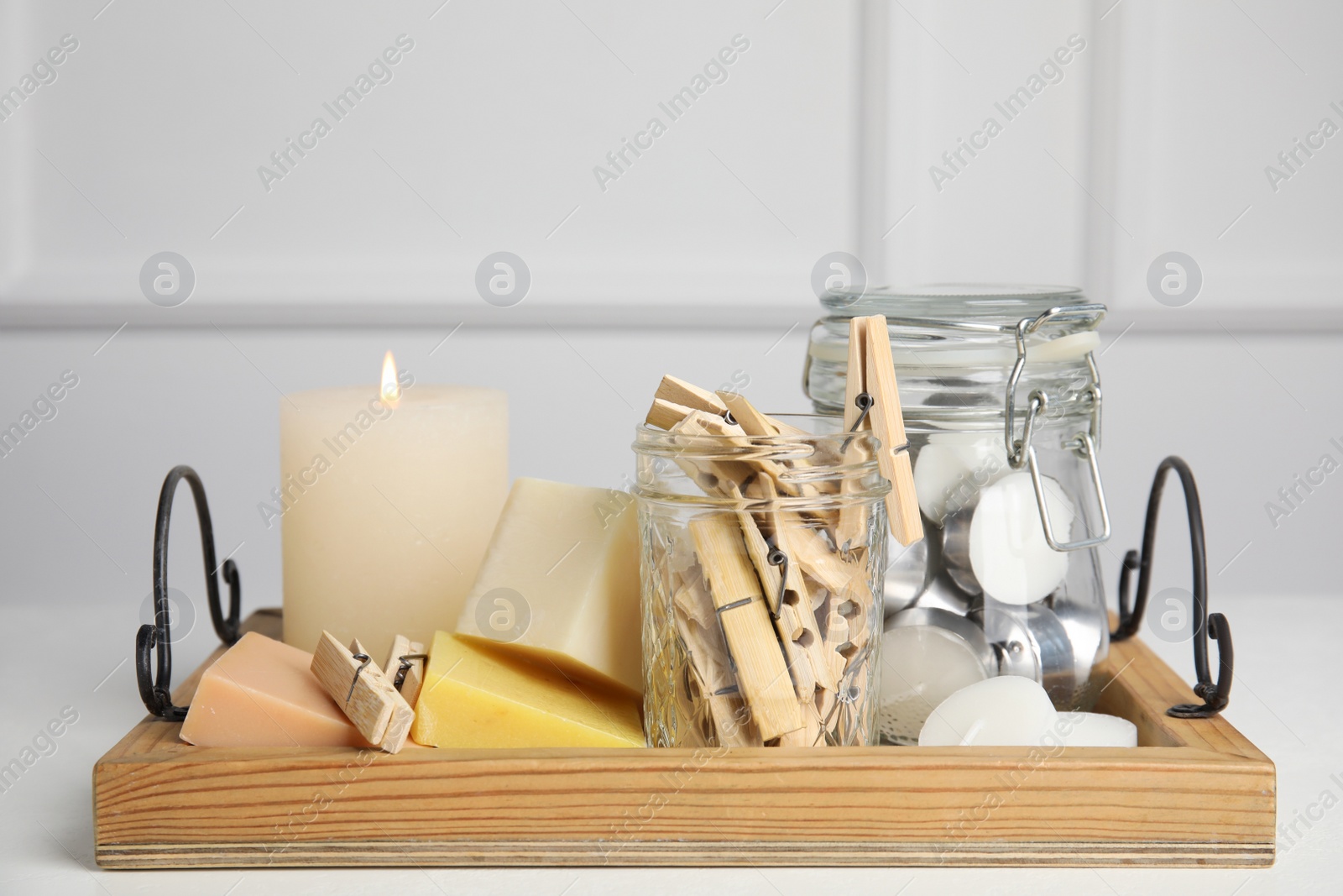 Photo of Wooden tray with many clothespins, candles and soap bars on white table