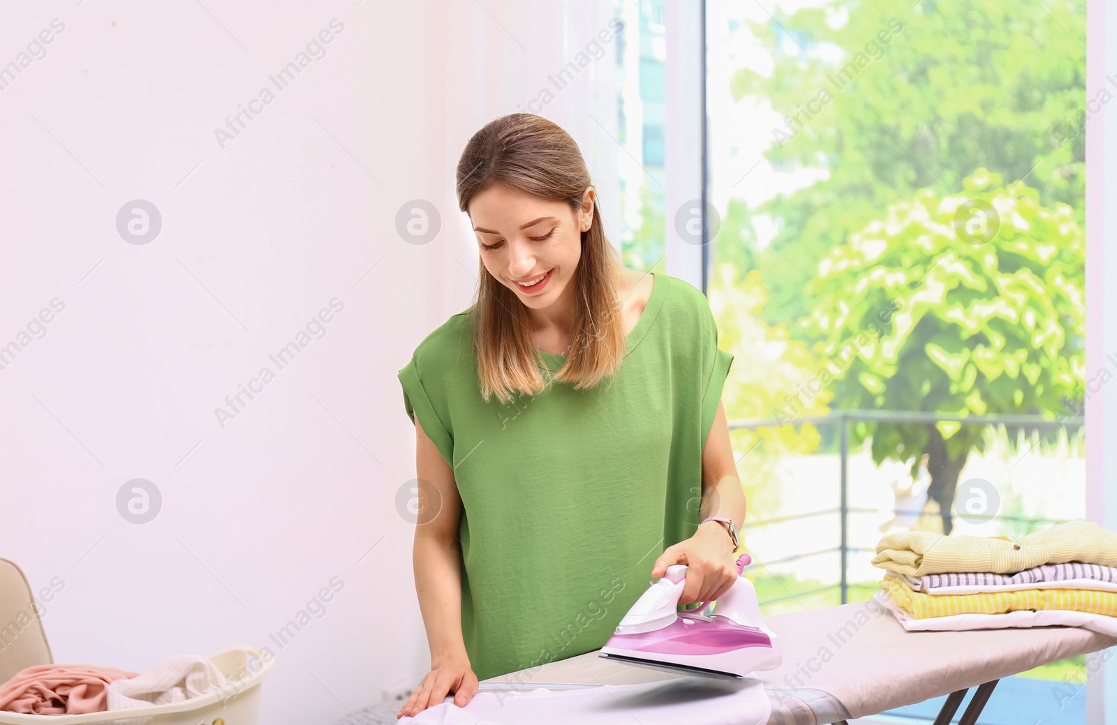 Photo of Young pretty woman ironing clean laundry indoors