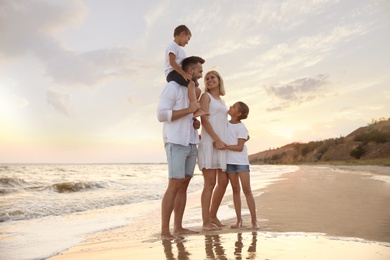 Happy family on sandy beach near sea at sunset