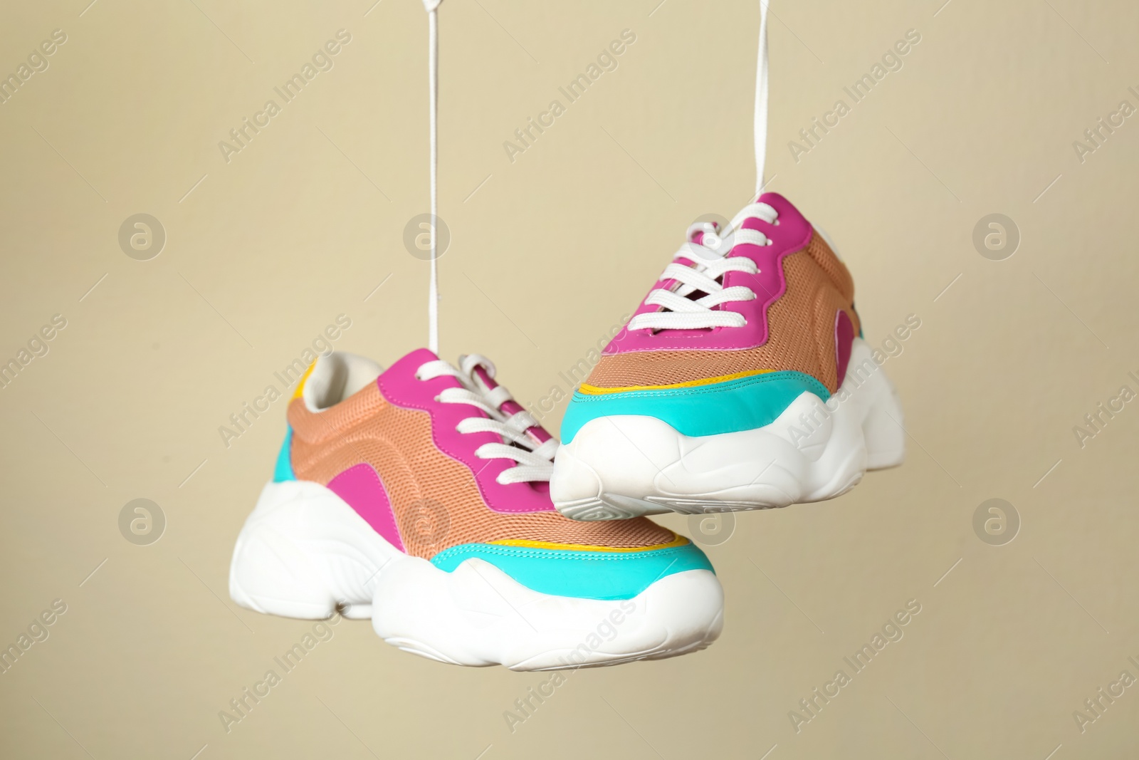 Photo of Stylish sports shoes hanging on beige background