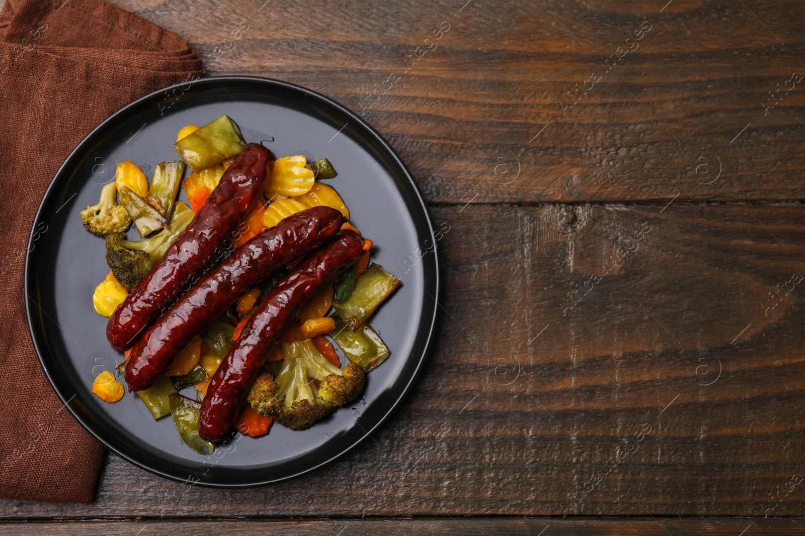 Photo of Delicious smoked sausages and baked vegetables on wooden table, top view. Space for text