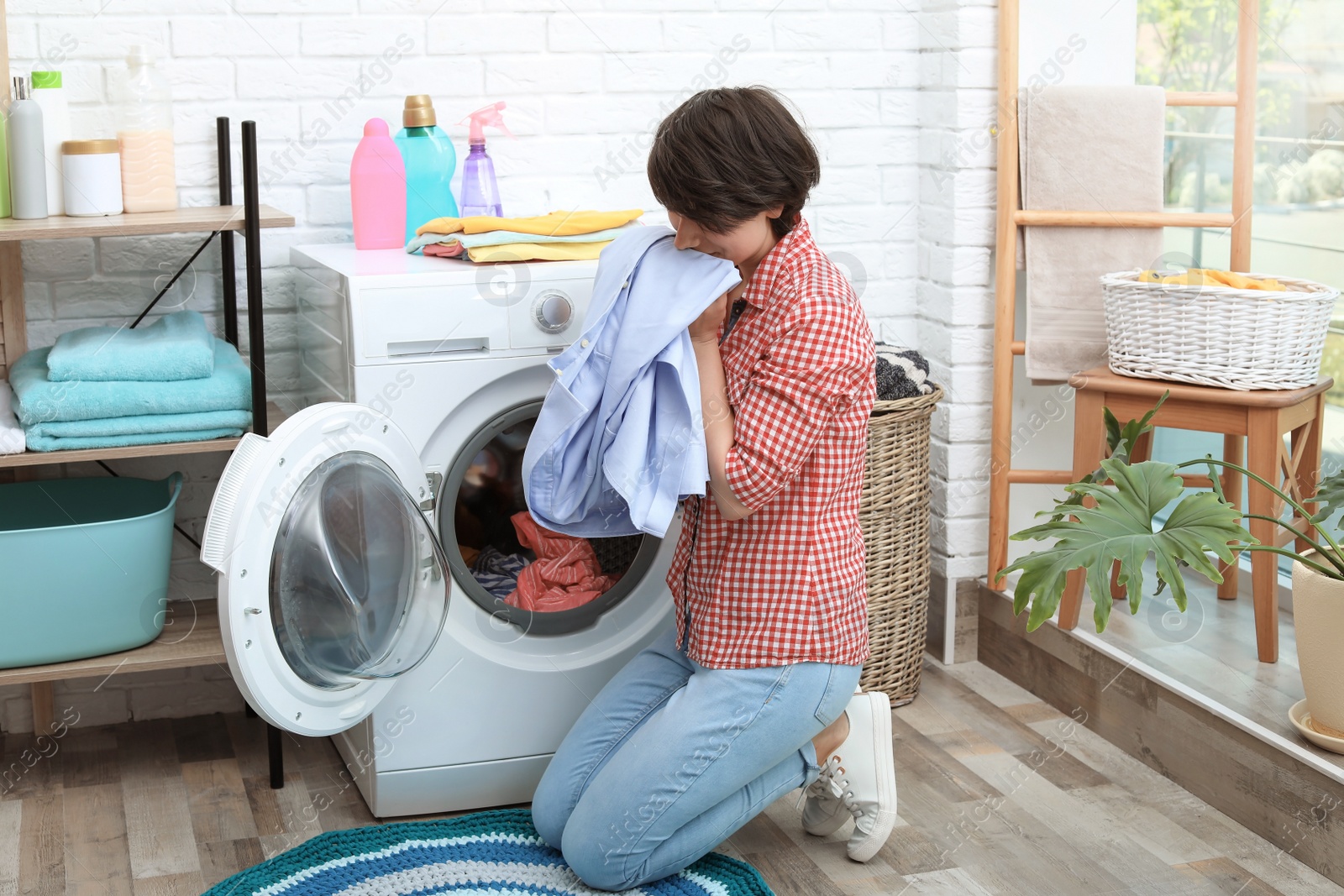 Photo of Young woman getting out clean clothes from washing machine at home