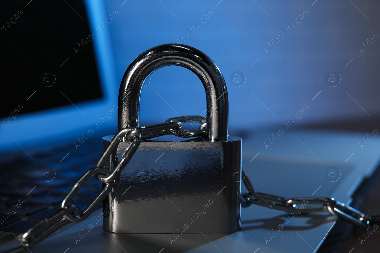 Photo of Cyber security. Laptop with padlock and chain on table, closeup