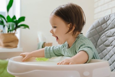 Cute little baby sitting in high chair indoors