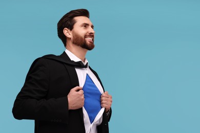 Photo of Happy businessman wearing superhero costume under suit on light blue background. Space for text